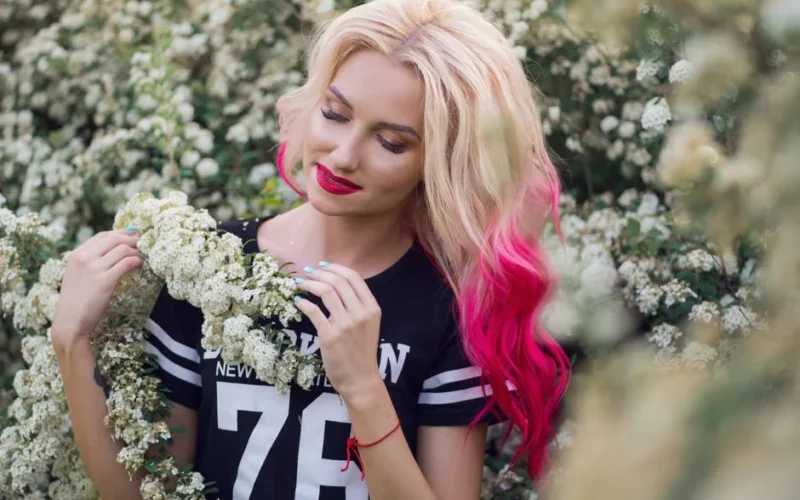 A beautiful woman with vibrant hair stands among blooming white flowers, creating a serene summer portrait.