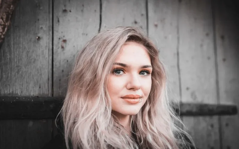 Portrait of a blonde woman with lip piercing against a wooden backdrop.