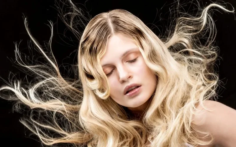 Stylish portrait of a woman with flowing blonde hair and closed eyes on a black background.